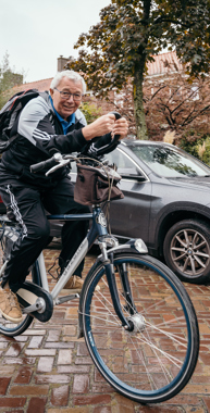 Wim van Vroonhoven op zijn fiets buiten in de straat. Wim van Vroonhoven (75) krijgt van inspanningsfysioloog Bart Vromans de juiste voorbereiding en begeleiding om zijn Individuele Senioren Kwart Triatlon te volbrengen.