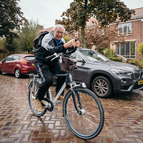 Wim van Vroonhoven op zijn fiets buiten in de straat. Wim van Vroonhoven (75) krijgt van inspanningsfysioloog Bart Vromans de juiste voorbereiding en begeleiding om zijn Individuele Senioren Kwart Triatlon te volbrengen.